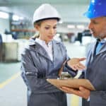 Man and woman wearing hard hats while going over information on a clipboard.