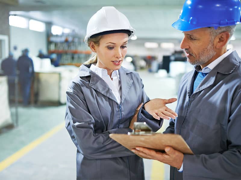 Man and woman wearing hard hats while going over information on a clipboard.
