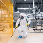 Exterminator in industrial plant spraying pesticide with sprayer.