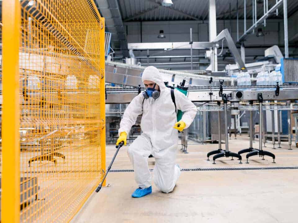 Exterminator in industrial plant spraying pesticide with sprayer.